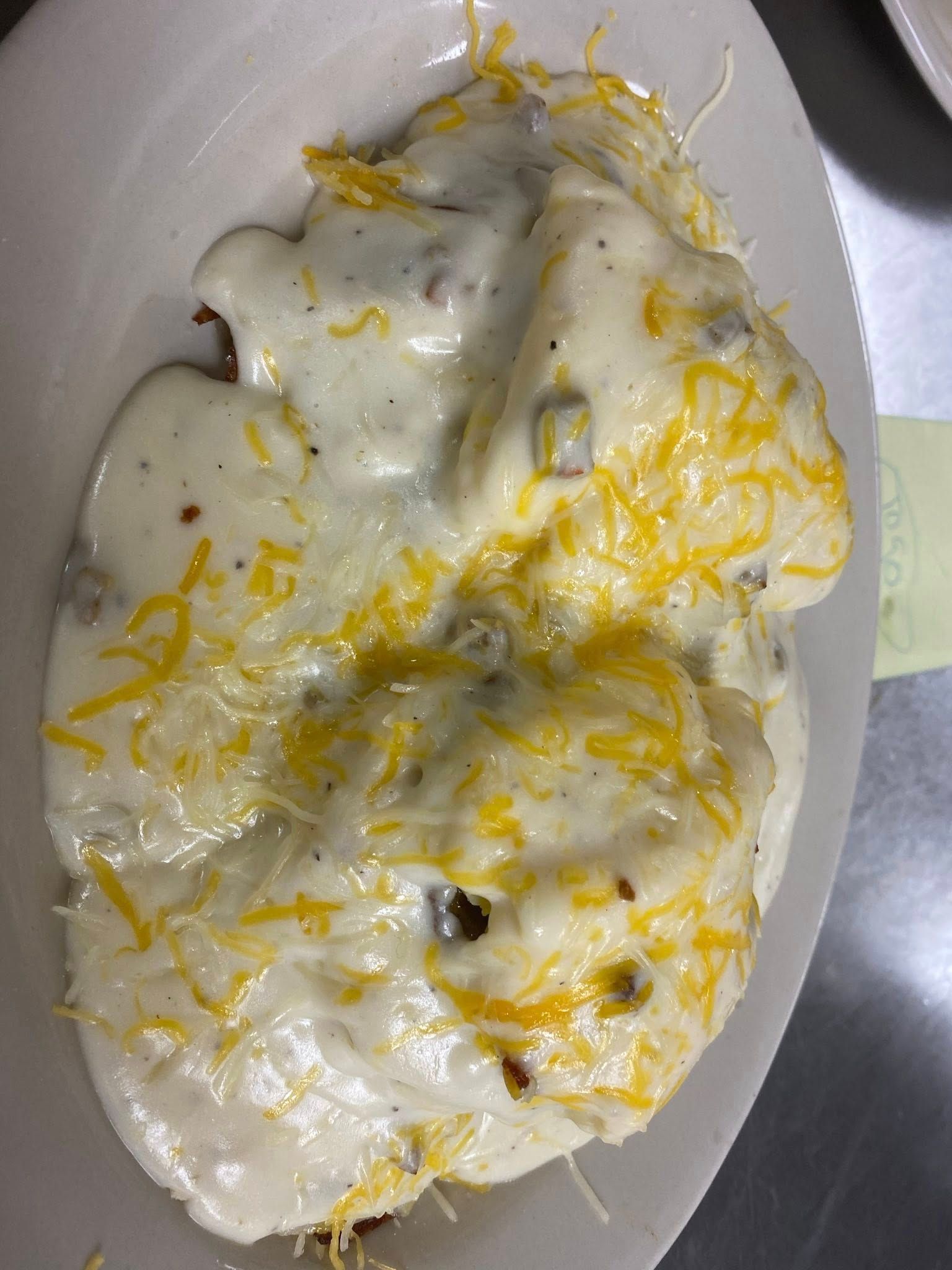 Biscuits smothered in sausage gravy and shredded cheddar cheese on a white plate.