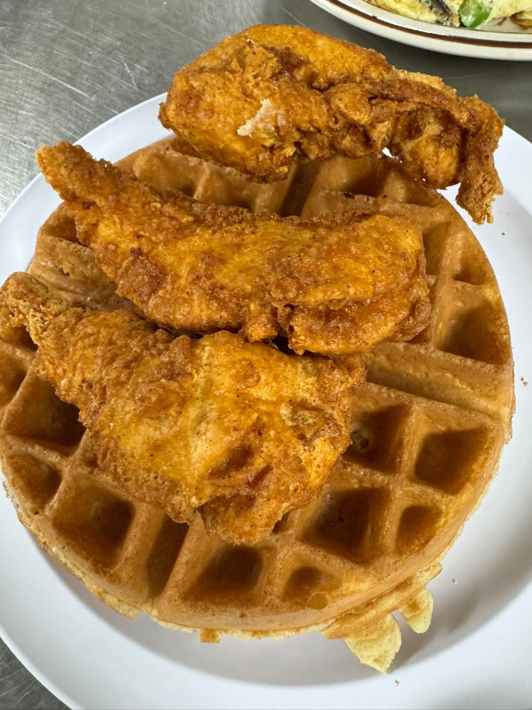 Fried chicken tenders on a waffle, served on a white plate.