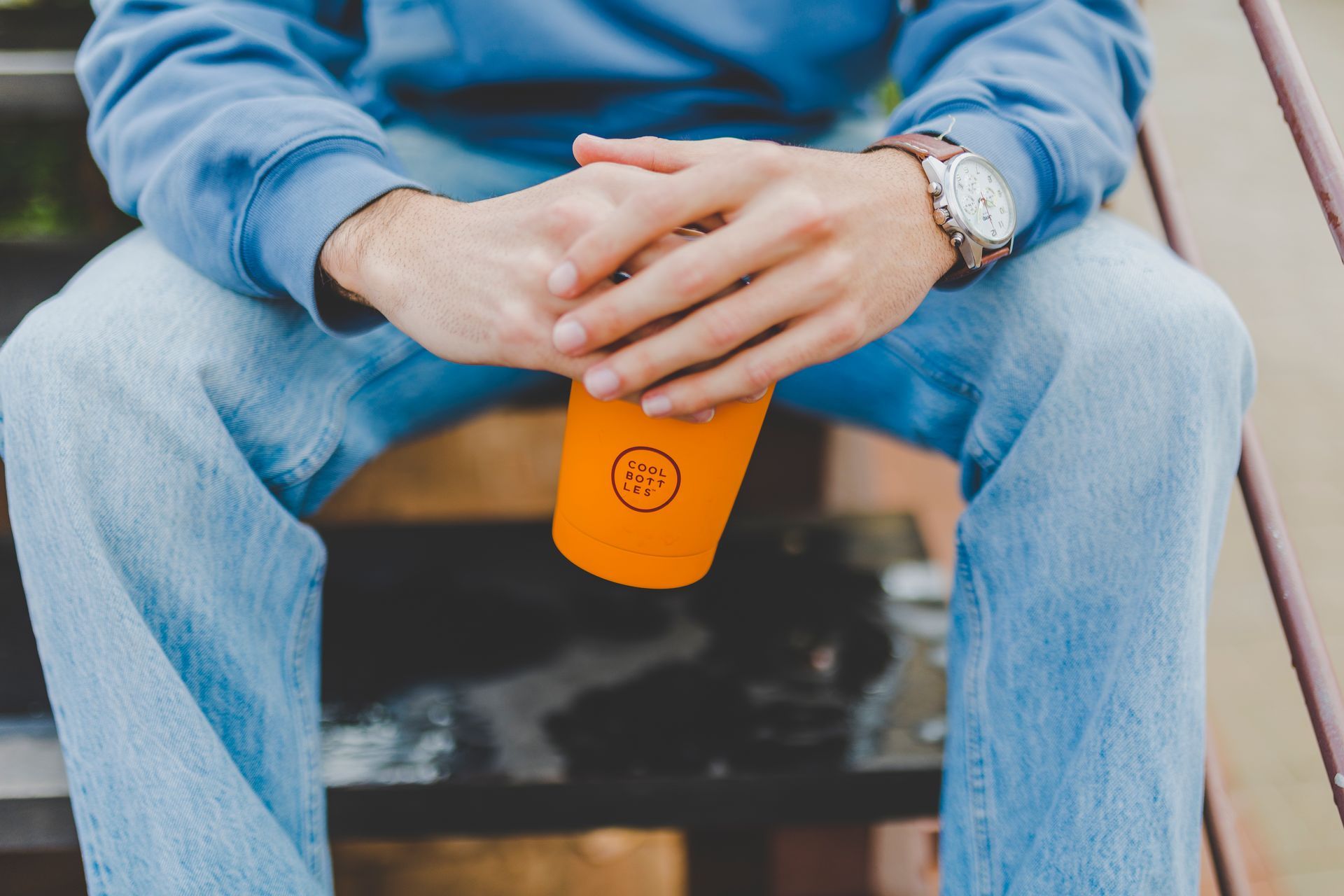 Rapaz sentado com um copo térmico laranja na mão