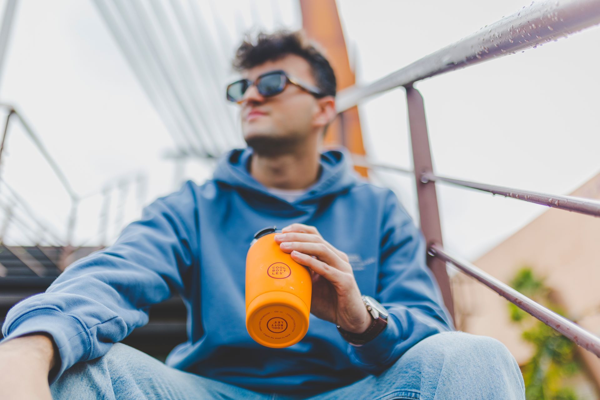 Homem sentado nas escadas com um copo térmico da Cool Bottles