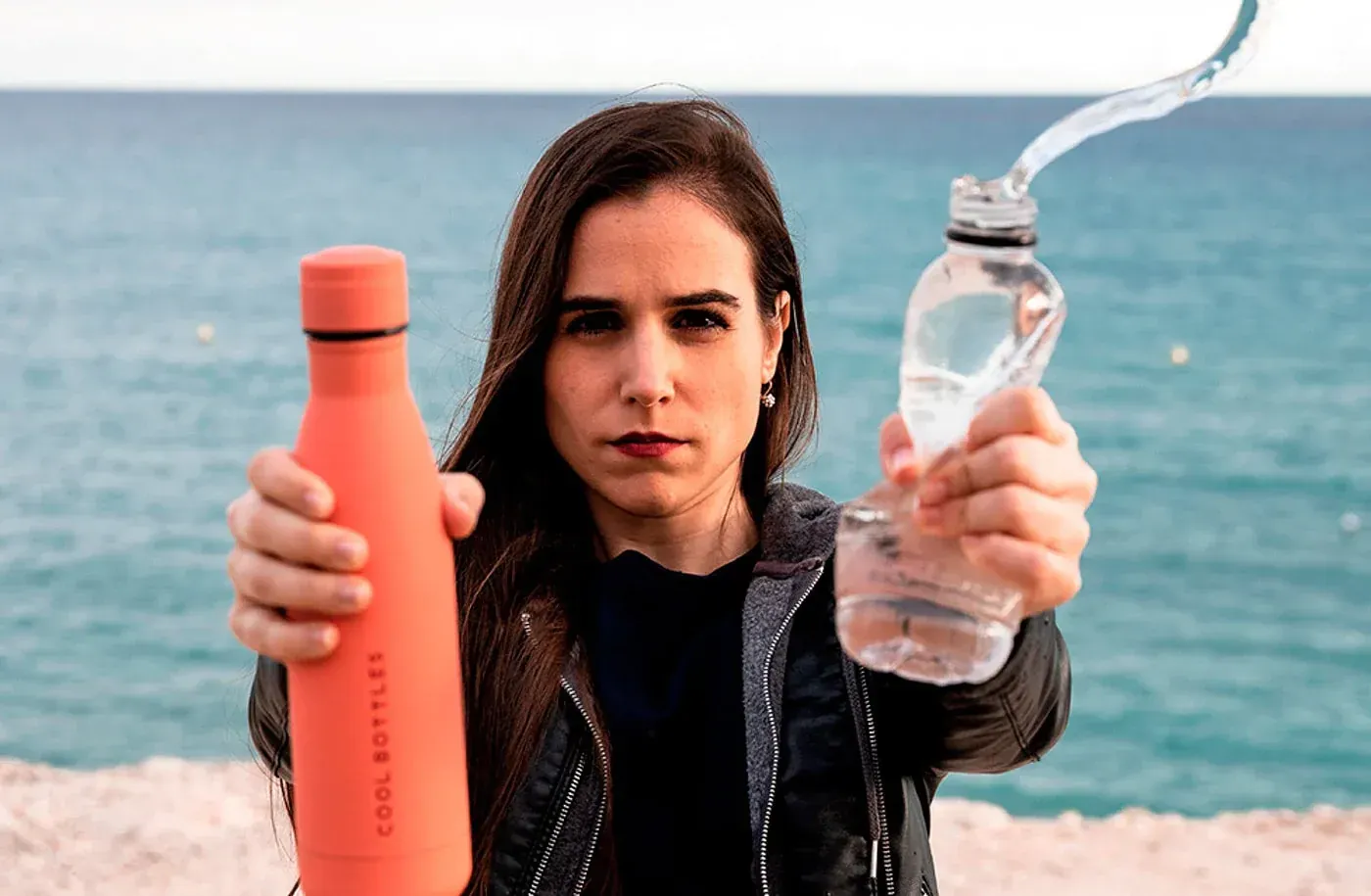 Mulher a apertar uma garrafa de plástico com uma mão e uma garrafa térmica da Cool Bottles com a outra
