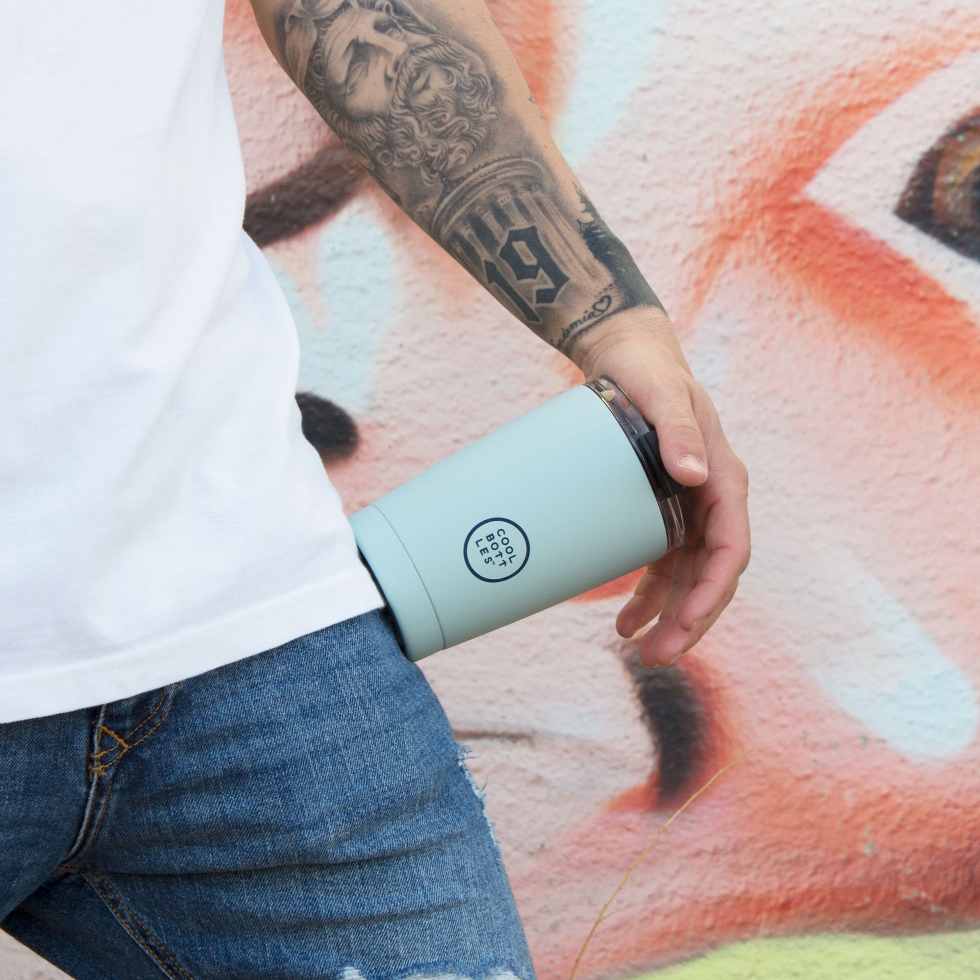 Jovem com tatuagens com um copo térmico azul claro da Cool Bottles
