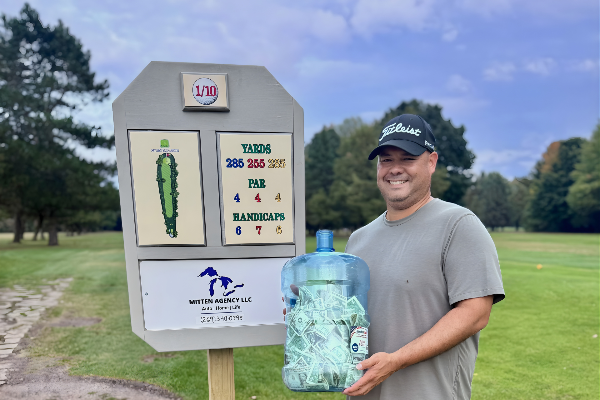 A smiling person stands on a golf course next to a hole marker, holding a large blue jug filled with golf tees.