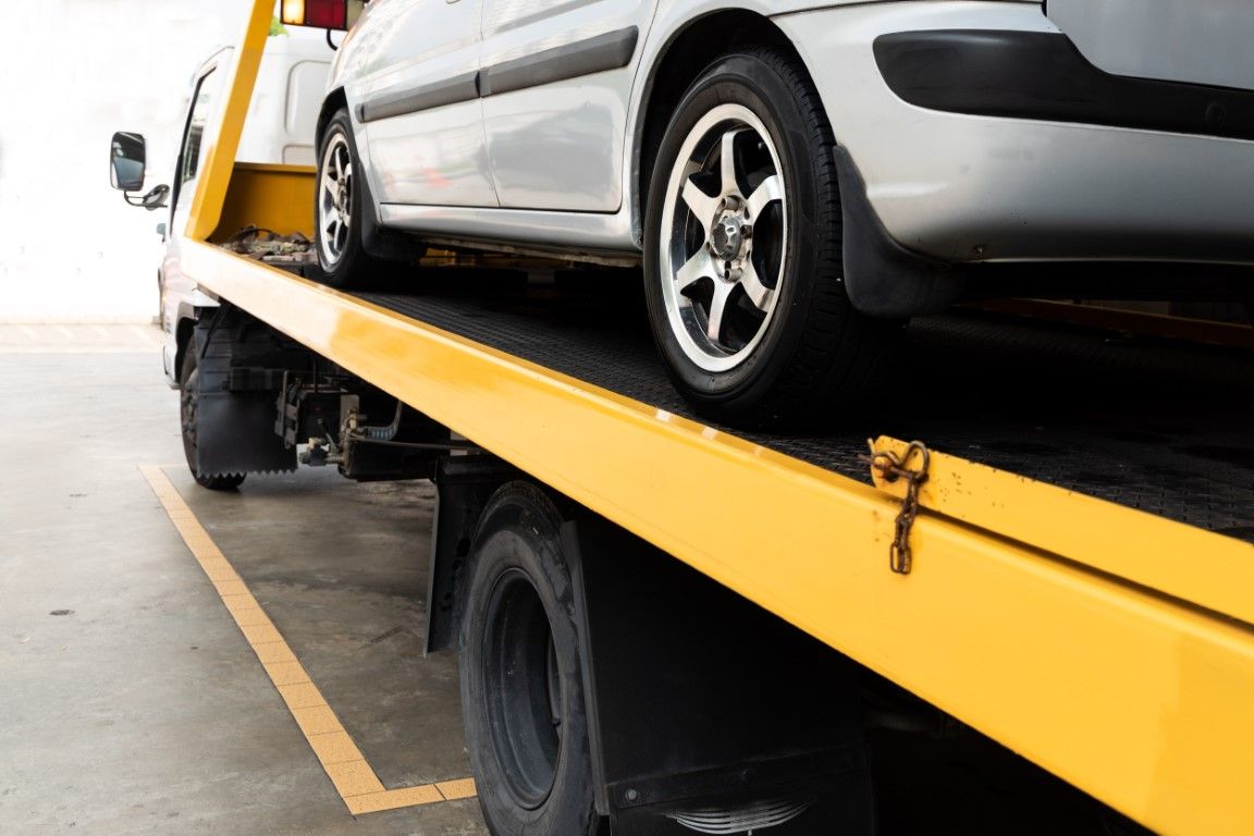 Silver car being towed on a yellow flatbed tow truck.