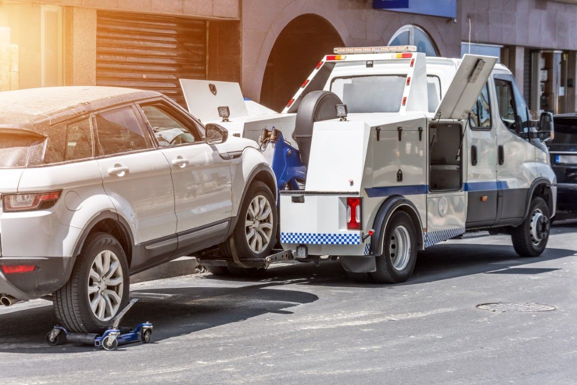 A white SUV being towed by a tow truck on a city street.