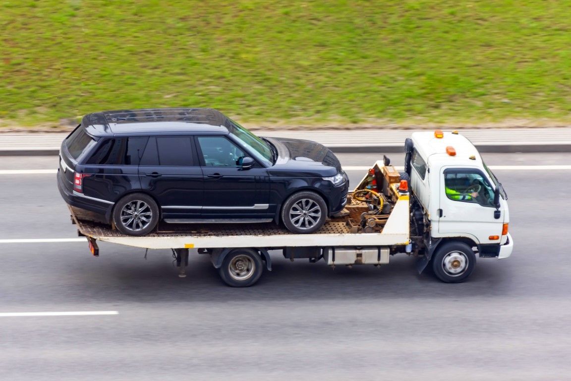 Black SUV being towed on a flatbed tow truck on a highway.