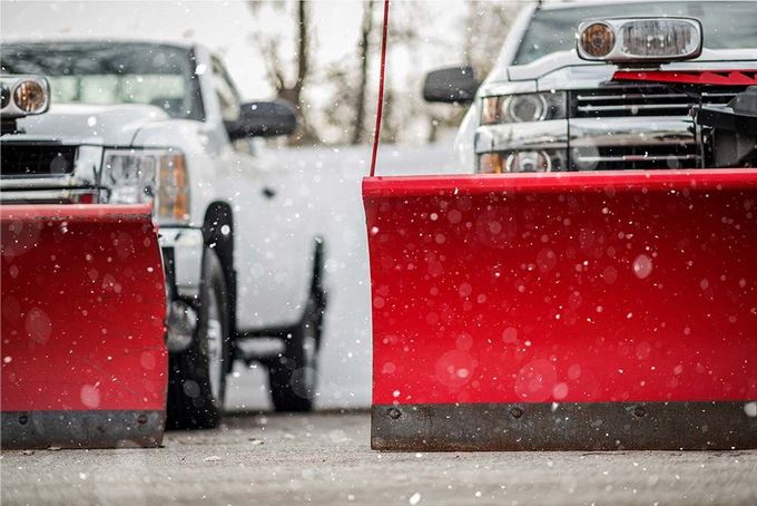 Two snow removal trucks with red snow plow blades set on pavement