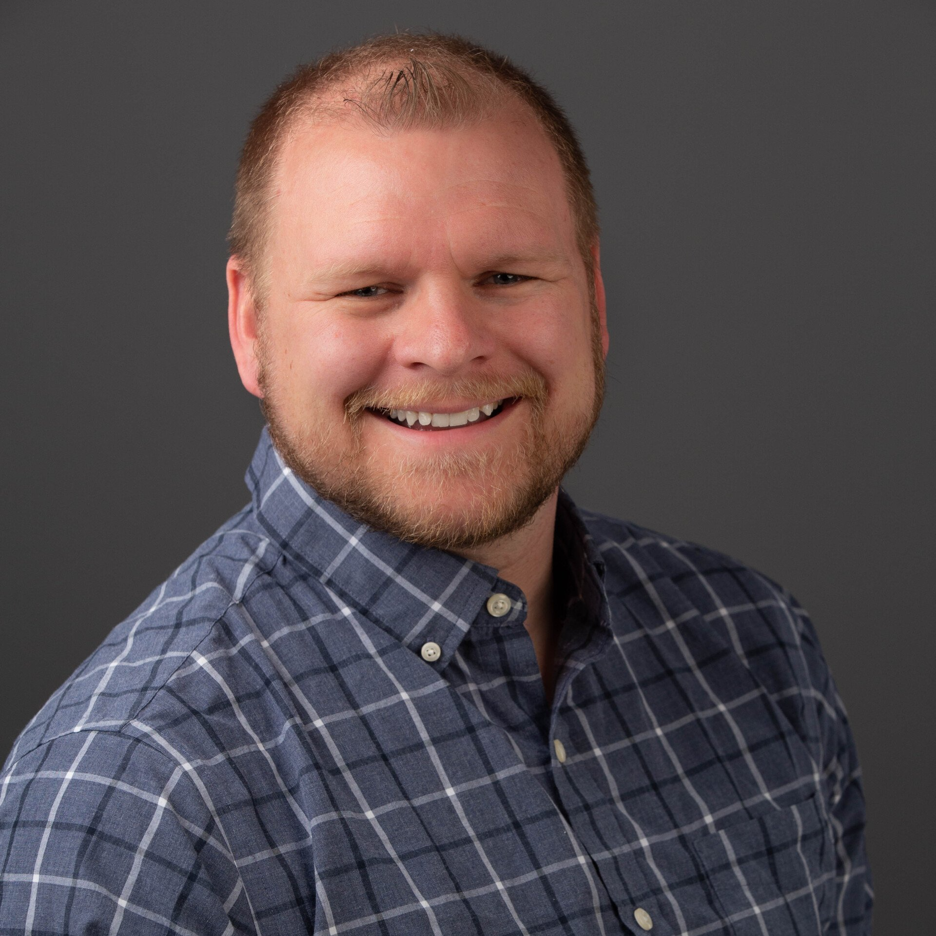 A man in a blue plaid shirt is smiling for the camera.