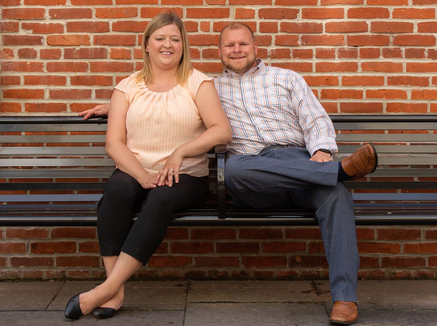 A man and a woman are sitting on a bench in front of a brick wall.