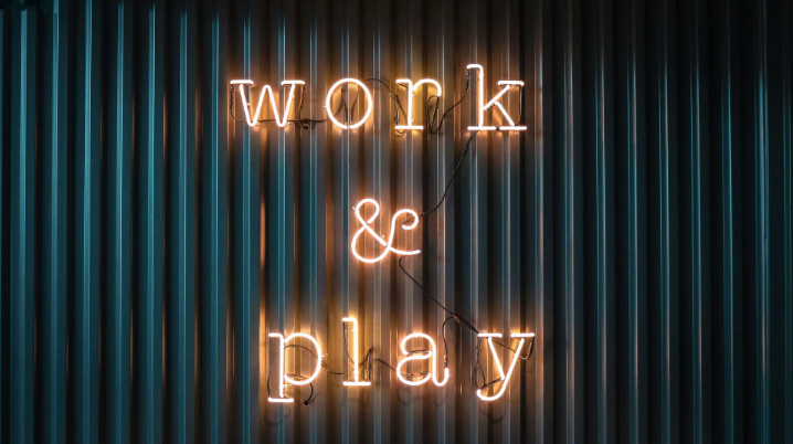 A neon sign that says `` work and play '' is lit up on a metal wall.