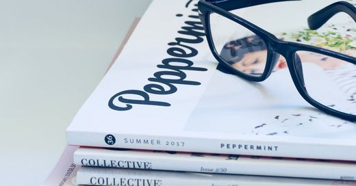 A pair of glasses sitting on top of a stack of magazines