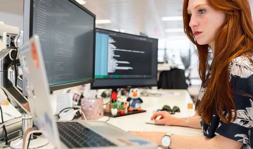 A woman is sitting at a desk looking at a computer screen.