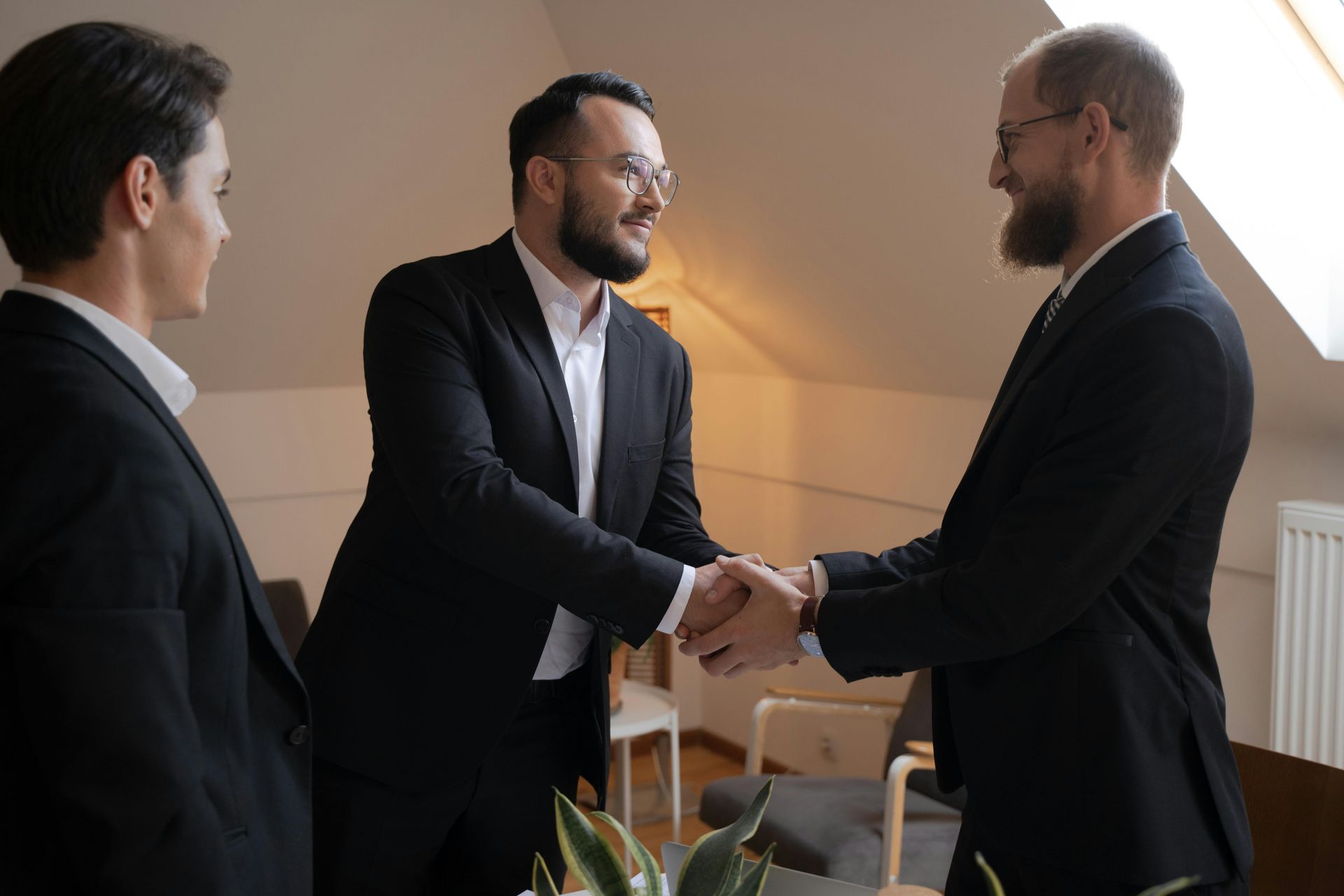 Three men in suits are shaking hands in a room.