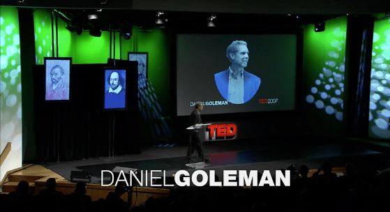 A man stands on a stage in front of a ted talk by daniel goleman