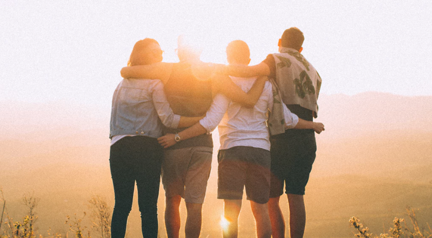 A group of people are hugging each other on top of a hill at sunset.