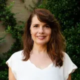 A woman in a white shirt is standing in front of a bush.