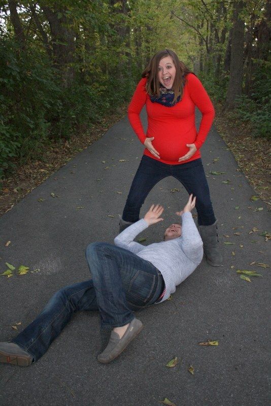 A pregnant woman is standing next to a man who is laying on the ground.