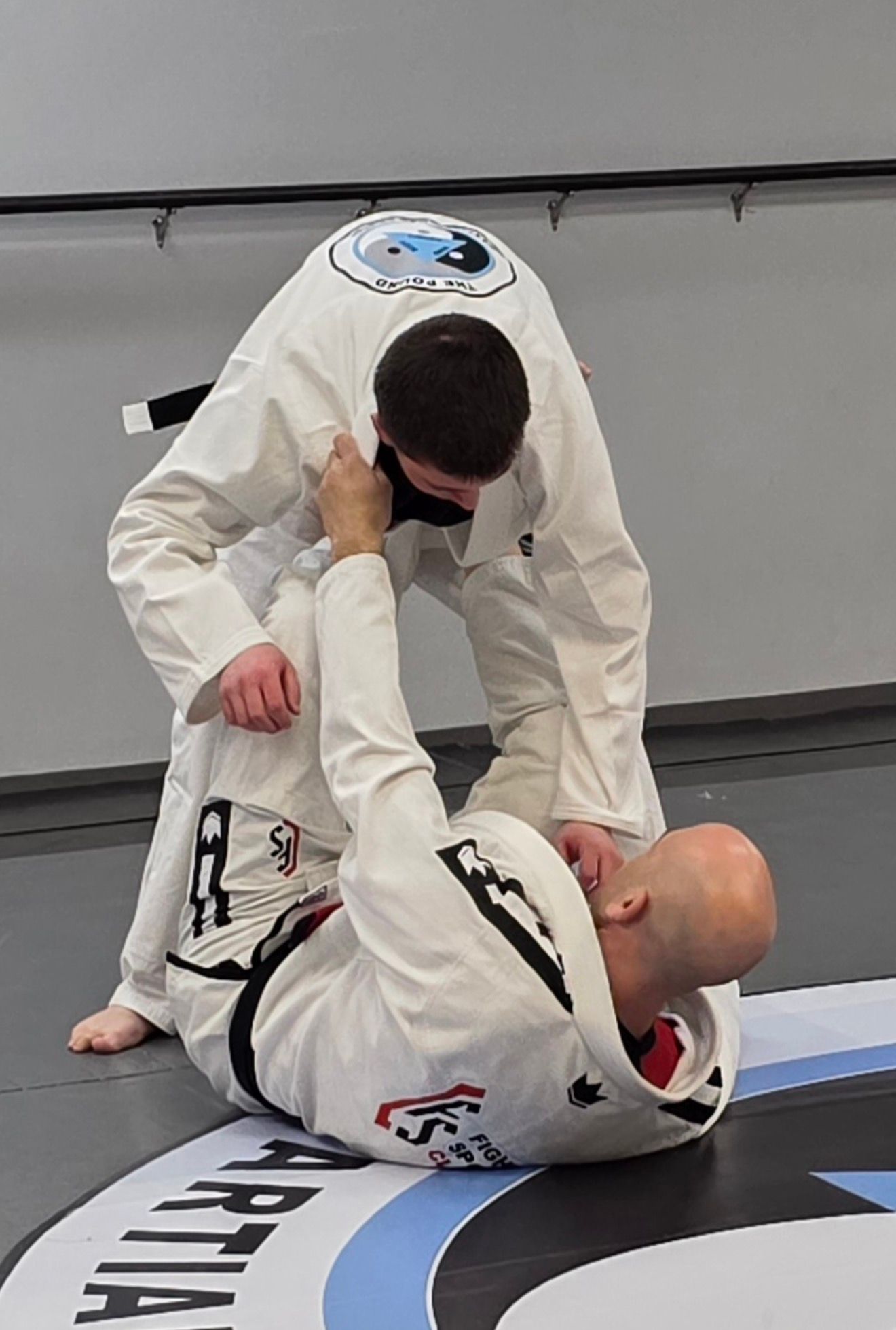 Group of children in martial arts attire posing, some with arms around each other, in a gym.