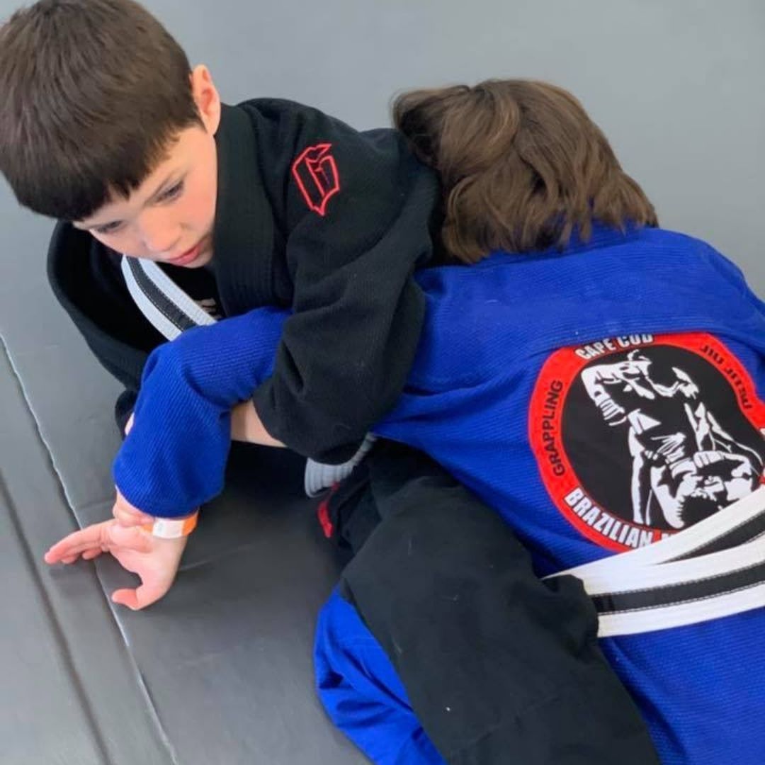 Five people in jiu-jitsu uniforms on a blue mat, including a man with a red belt, posing in a gym.