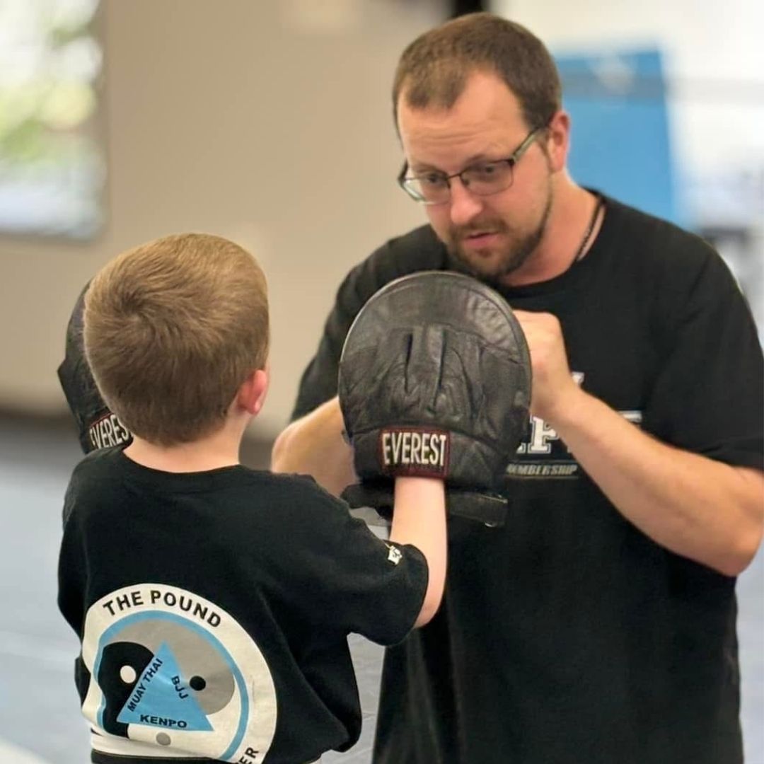 People practicing Brazilian Jiu-Jitsu. One person on the ground, another on top; two others grappling nearby. Black gis, indoor setting.