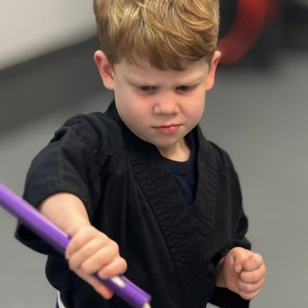 Two children grappling on a mat, one in a headlock.