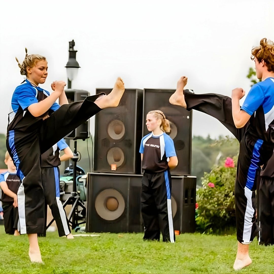 Group of children in martial arts attire posing, some with arms around each other, in a gym.
