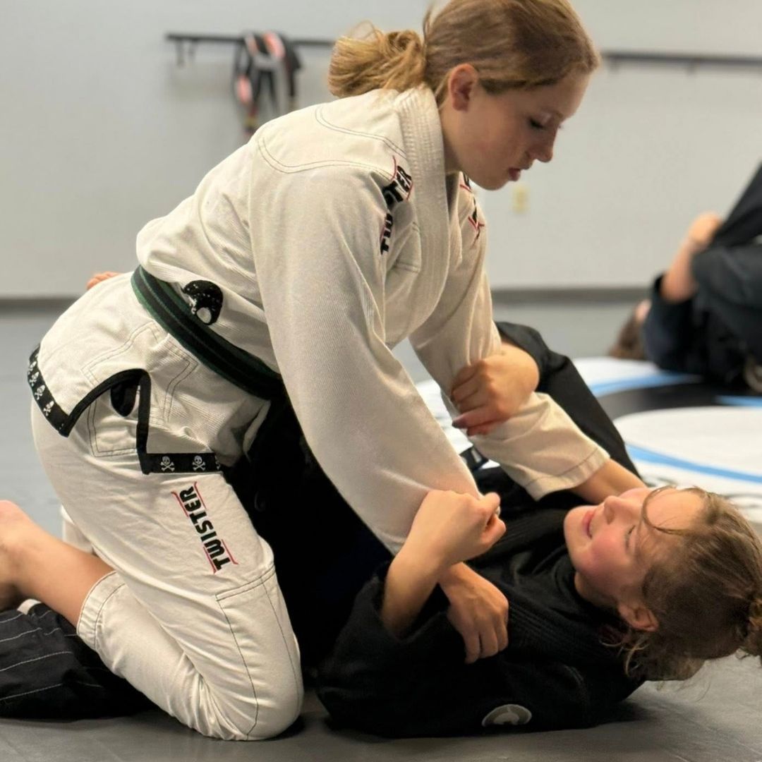 Five people in jiu-jitsu gear pose together in a gym.  Smiling,  some have arms around each other. Machado logo visible.