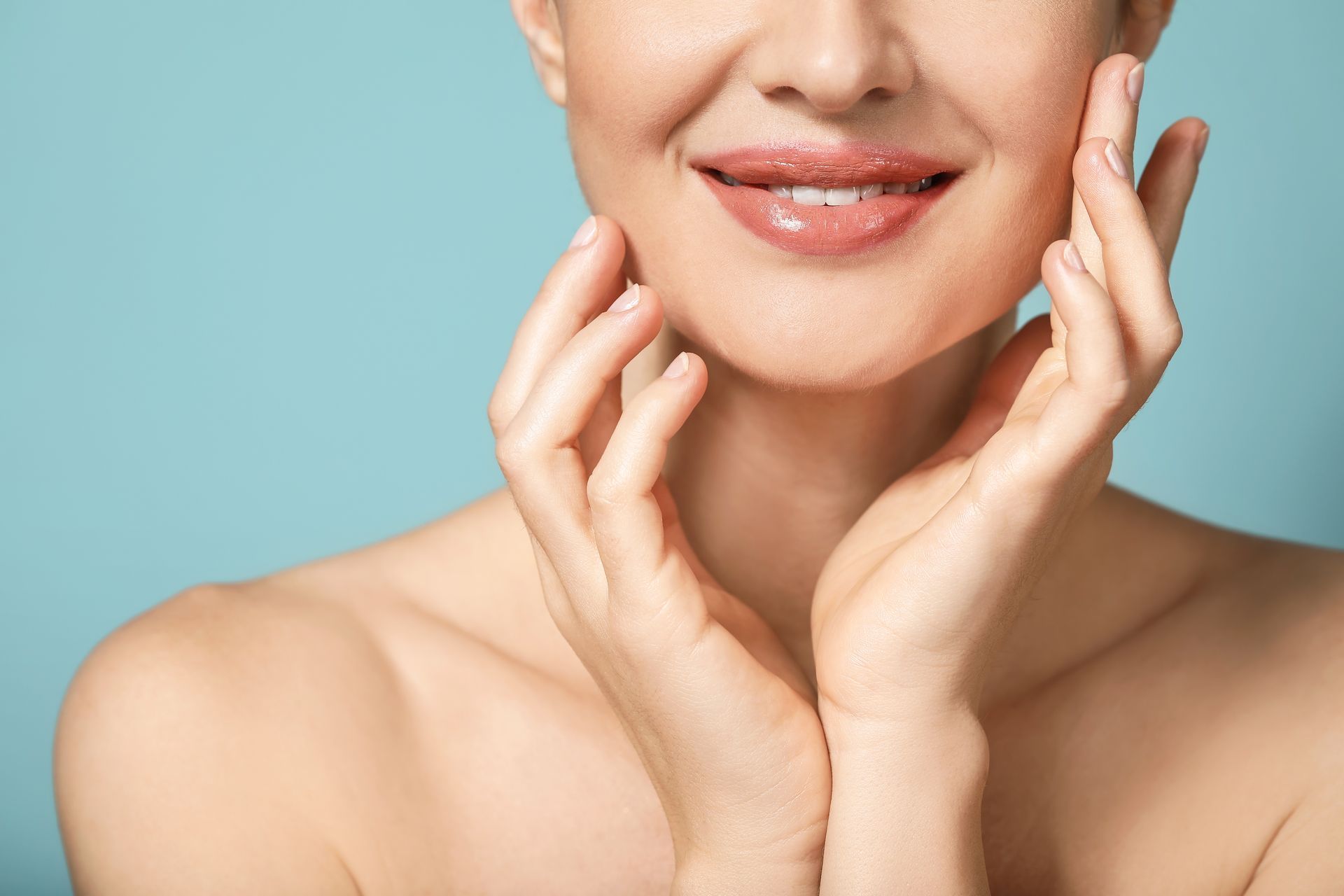 Smiling person with hands touching cheeks against a blue background, shoulders visible.