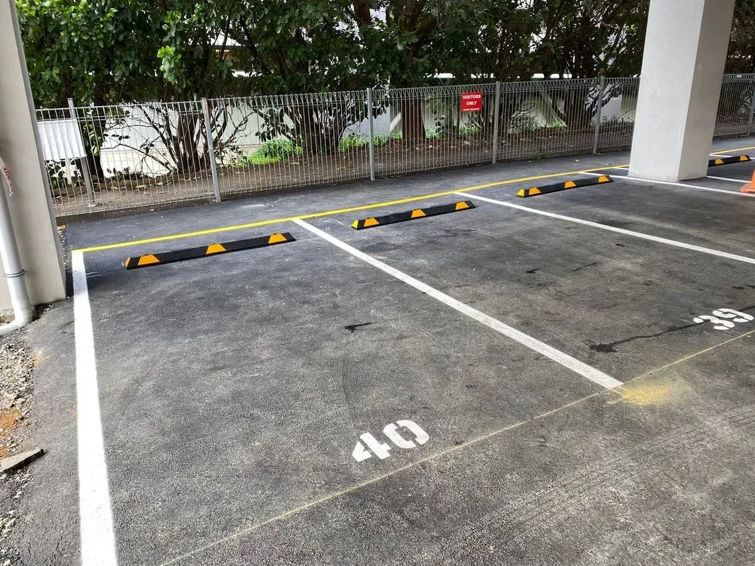 Parking spaces numbered 39 and 40 with wheel stops. Asphalt surface, white lines, gray pillar, and greenery in background.