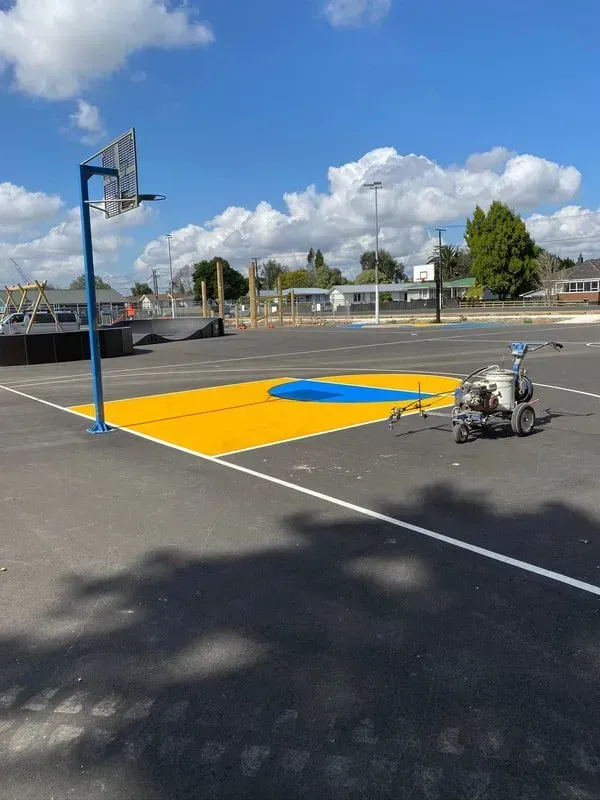 Yellow painted basketball court with blue key, being painted on asphalt, blue sky.