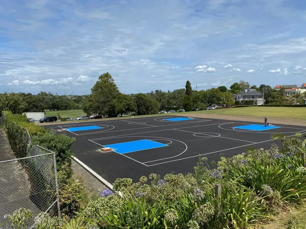 Playground with black surface, blue markings, and trees under a blue sky.