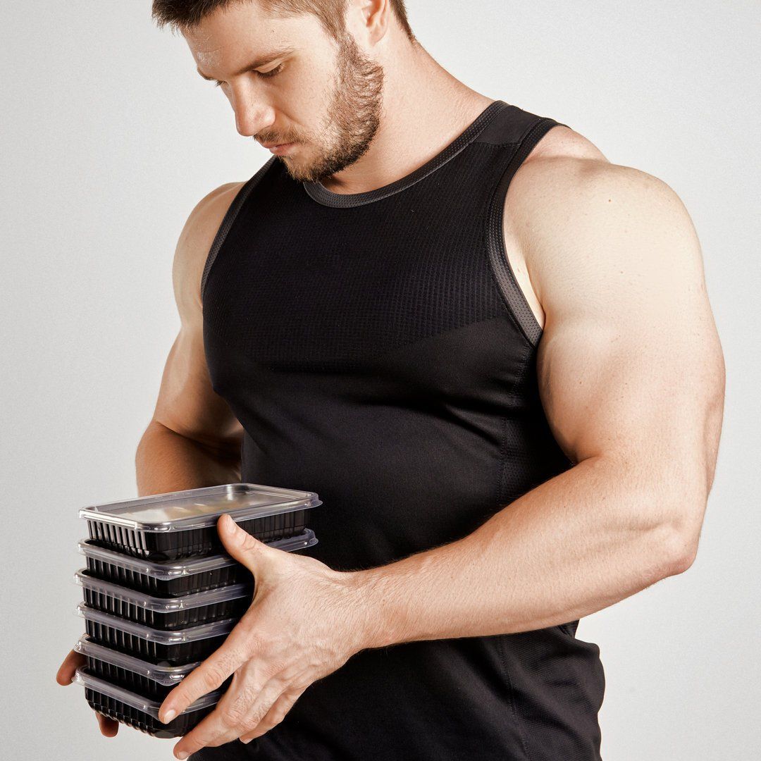 A man in a black tank top is holding a stack of plastic containers