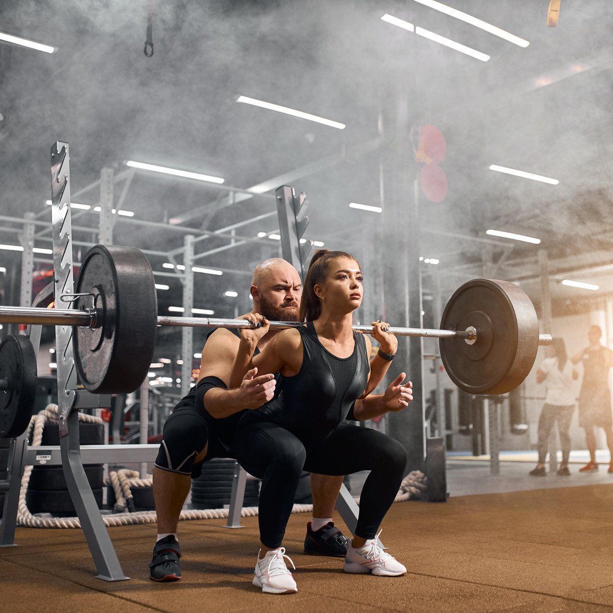 A man and a woman are squatting with a barbell in a gym.