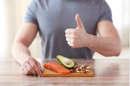A man is giving a thumbs up while cutting a piece of salmon on a cutting board.