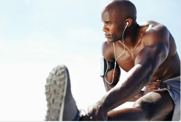 A shirtless man is stretching his legs while listening to music