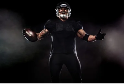 A football player in a black uniform is holding a football in his hands.