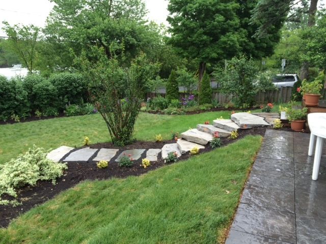 Une cour verdoyante avec une allée en pierre menant à un patio.