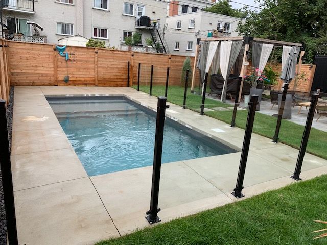 Une piscine est entourée d'une clôture en verre dans une cour arrière.