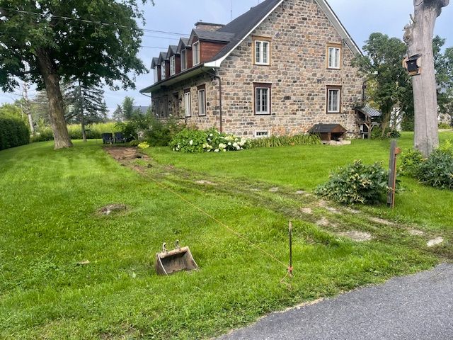 Une grande maison en pierre est située au sommet d'un champ verdoyant.
