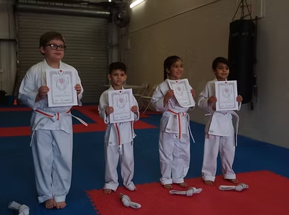 A group of children in karate uniforms are holding certificates in a gym.