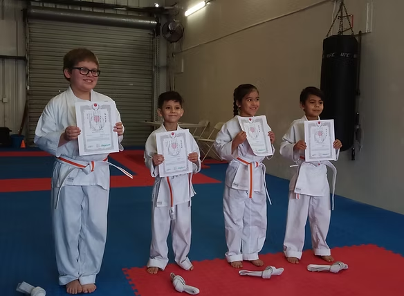 A group of kids in karate uniforms are holding up certificates