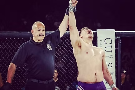 A referee is holding up a shirtless fighter 's hand in a boxing ring.