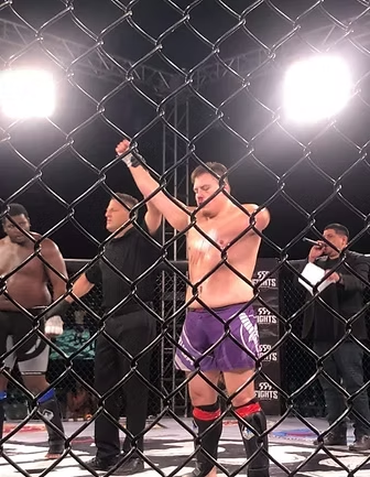 A man in purple shorts is standing behind a chain link fence.