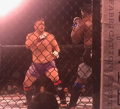 Two men are fighting in a cage with a sign that says fabrication steel