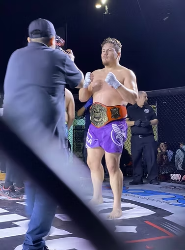 A man is standing in a boxing ring with a belt around his waist.