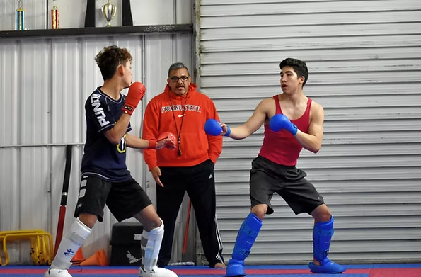 Two men are boxing in a gym with a coach watching.
