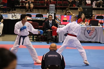 Two karate fighters are fighting on a mat with a referee watching