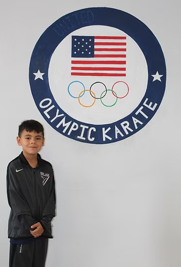 A young boy stands in front of an olympic karate logo