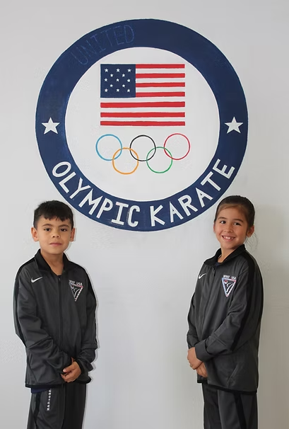 A boy and a girl stand in front of an olympic karate logo