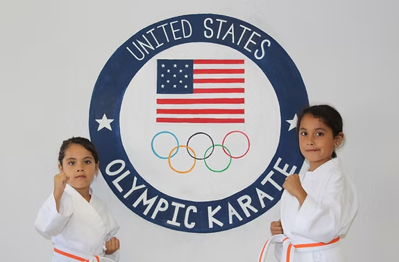 Two young girls standing in front of a united states olympic karate logo